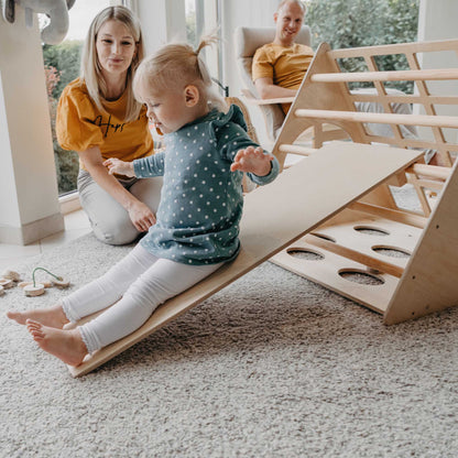 A child is playing with a climbing triangle with sensory panels in a living room, using a balance beam.