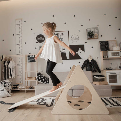 A little girl is playing with a climbing triangle with sensory panels in her living room.