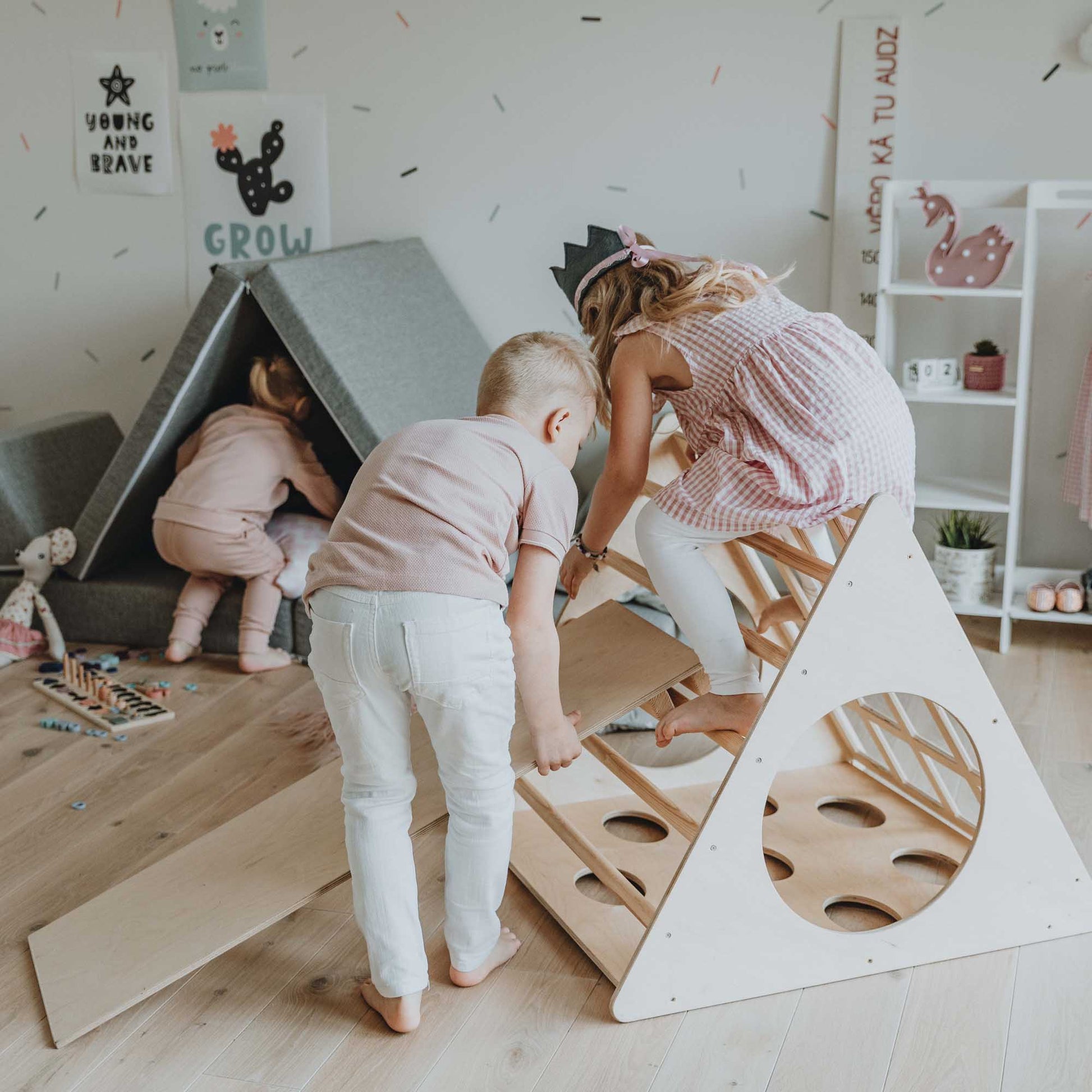 Two children engaging in Montessori play with a climbing triangle with sensory panels, honing their motor skills as they climb a small ladder in the playroom.