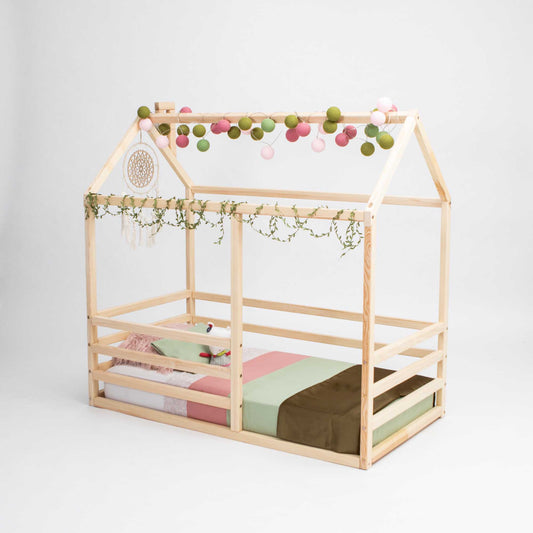 A floor level house bed with a horizontal fence for toddlers with a wooden frame and netting, providing a montessori floor level sleeping experience for kids.
