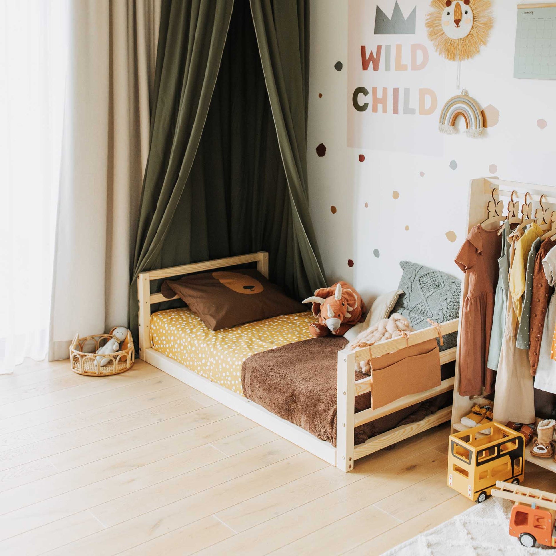 A child's room with a Sweet Home From Wood toddler floor bed adorned with adorable sheets, along with an assortment of clothes and toys to keep any child.