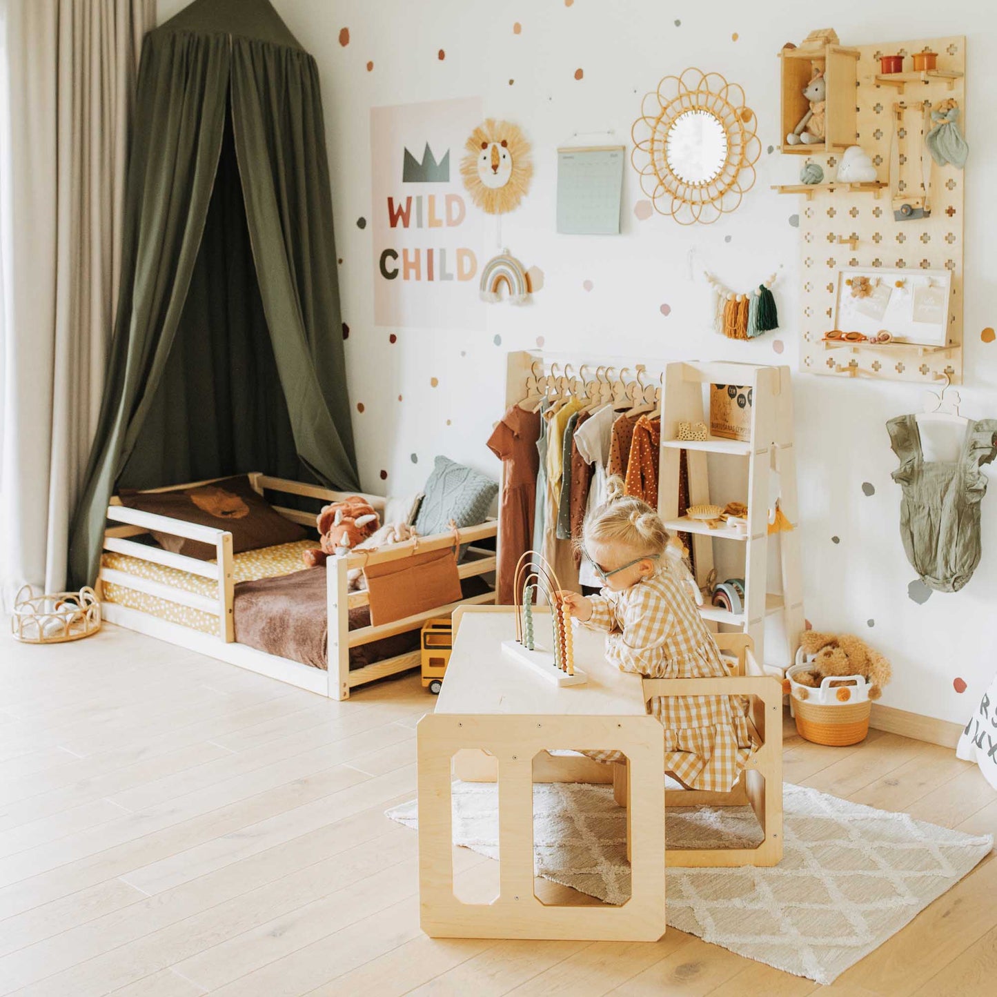 A child's room with a wooden desk and a canopy, featuring the Sweet Home From Wood's floor-level kids' bed with a horizontal rail fence, providing an independent sleeping area for children.