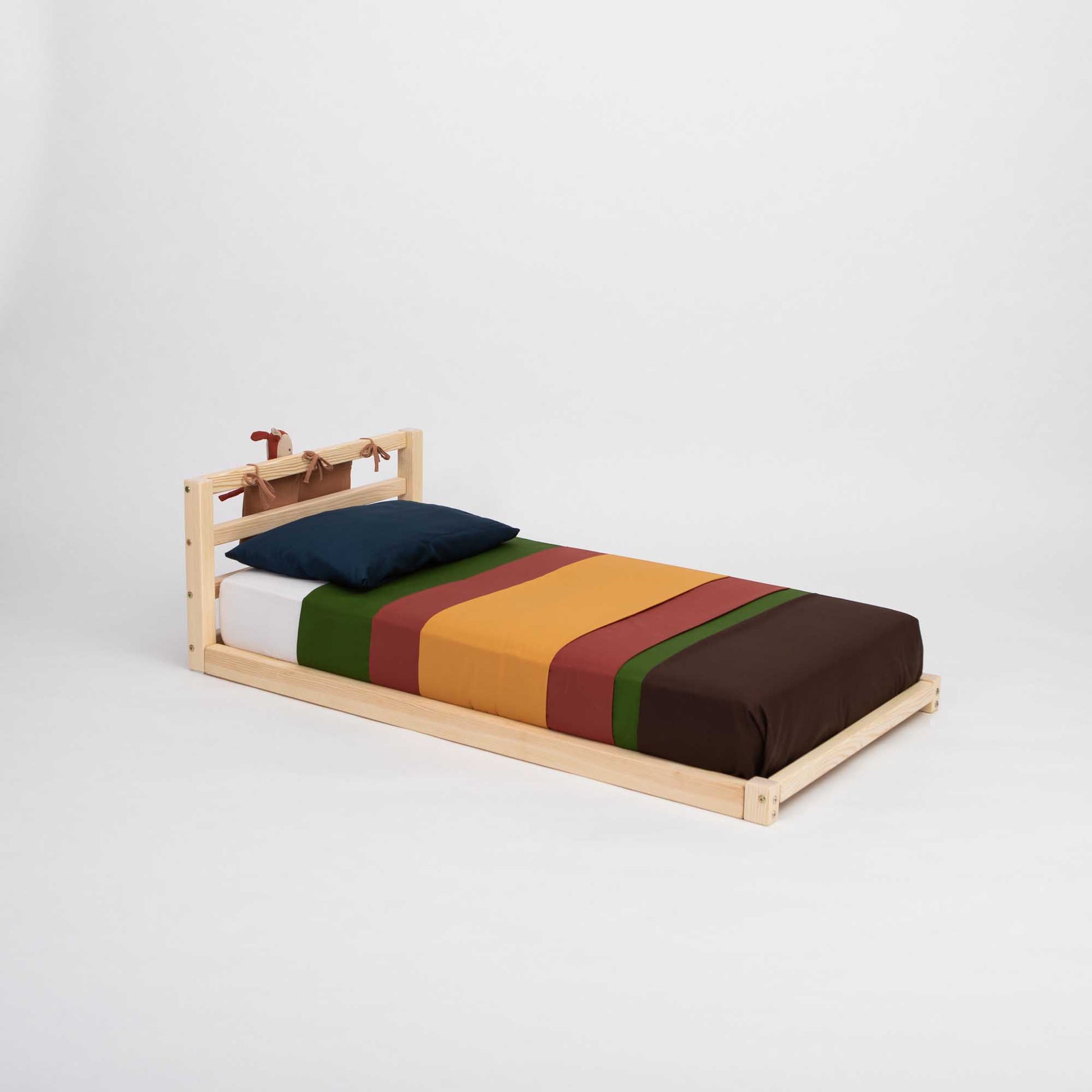 A Sweet Home From Wood toddler floor bed with a horizontal rail headboard and a colorful striped sheet.