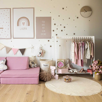 A girl's room with an A-frame kids' clothing rack and clothing storage in pink and white decor.