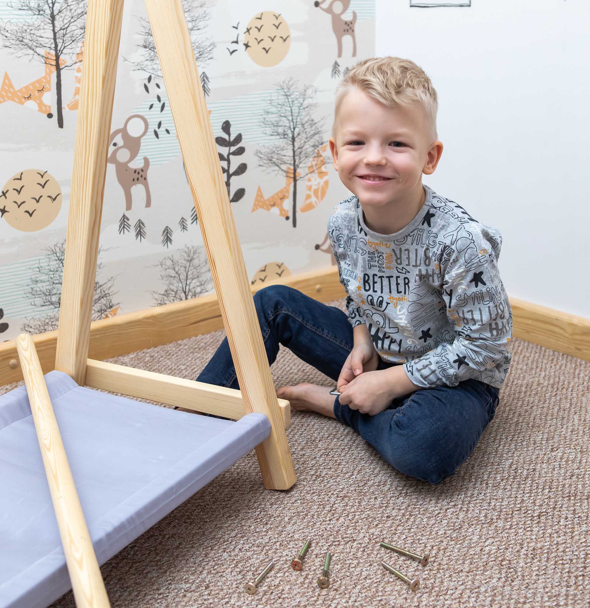 A young boy sitting on the floor with a Sweet Home From Wood Kids' clothing rack with storage.