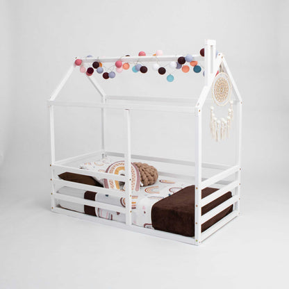 A floor level house bed with a horizontal fence and pom poms hanging from it.