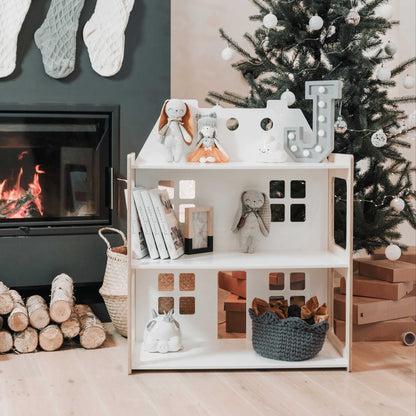A 2-in-1 doll house and Montessori shelf from Sweet Home From Wood on an open toy storage shelf in front of a fireplace.