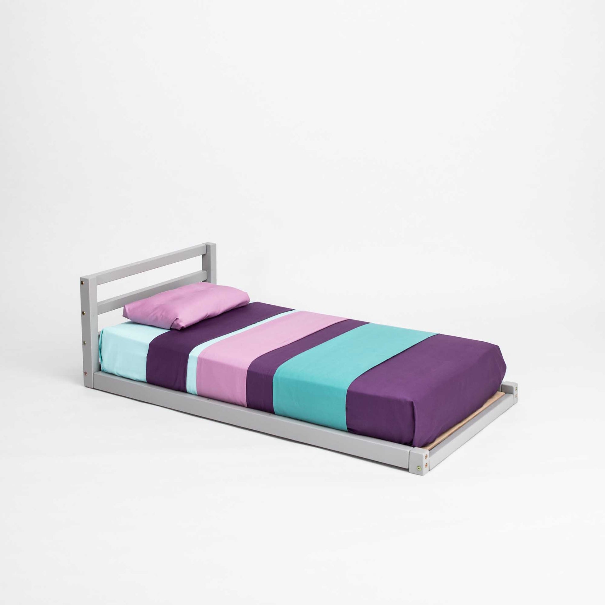 A Sweet Home From Wood toddler floor bed with a horizontal rail headboard, with a purple, blue, and green striped sheet.
