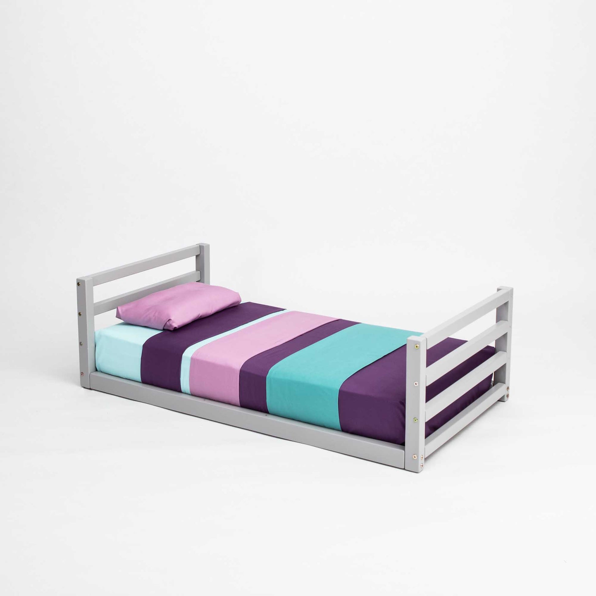 A Sweet Home From Wood toddler floor bed with a horizontal rail headboard and footboard, with a purple, blue, and green striped sheet.