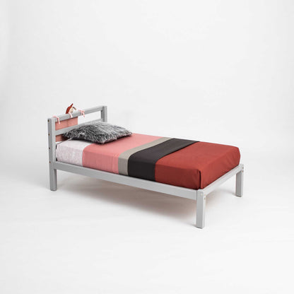 A small Sweet Home From Wood kids' bed on legs with a horizontal rail headboard and a red, black, and grey cover.