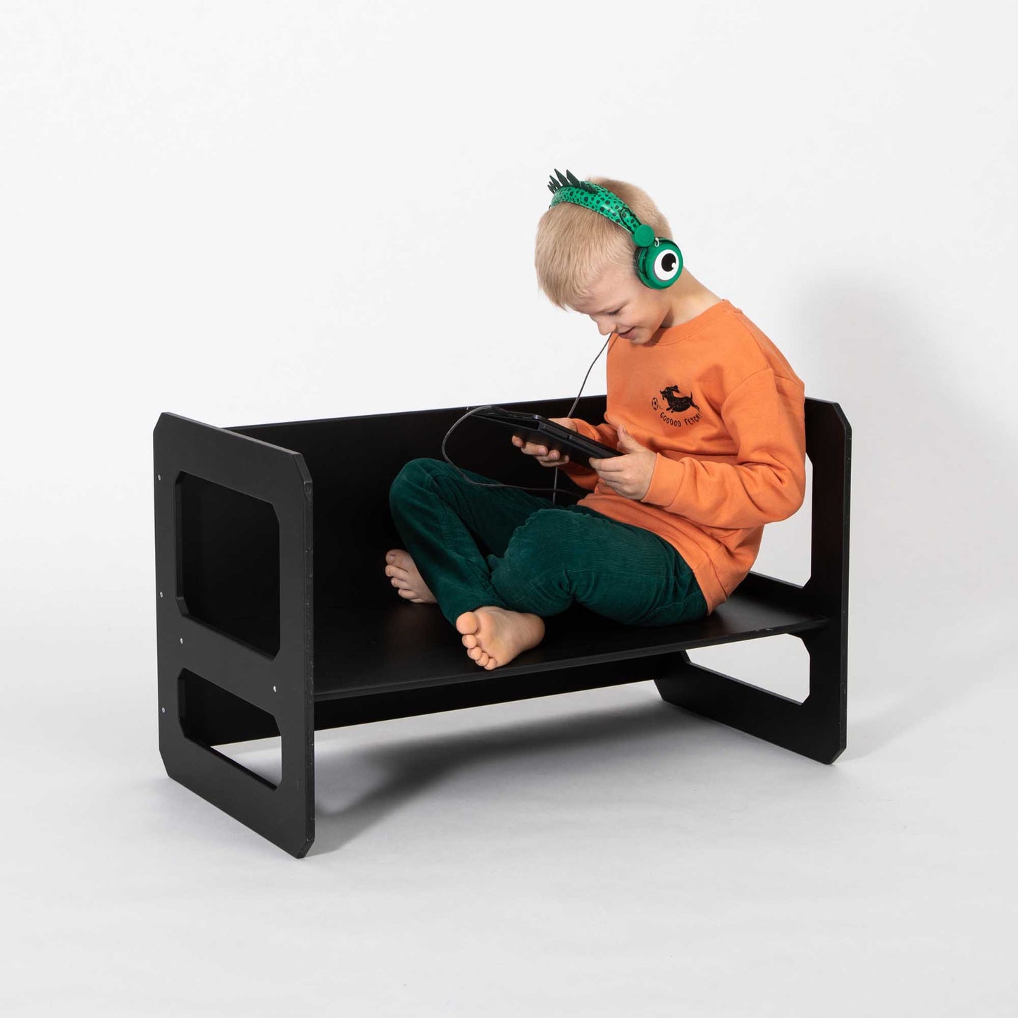 A young boy sitting on a black bench with headphones, enjoying the comfort of the Sweet Home From Wood Montessori weaning table.