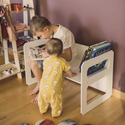 Two children sitting on a white bench in a child's room, engrossed in reading books at their Sweet Home From Wood Montessori weaning table.