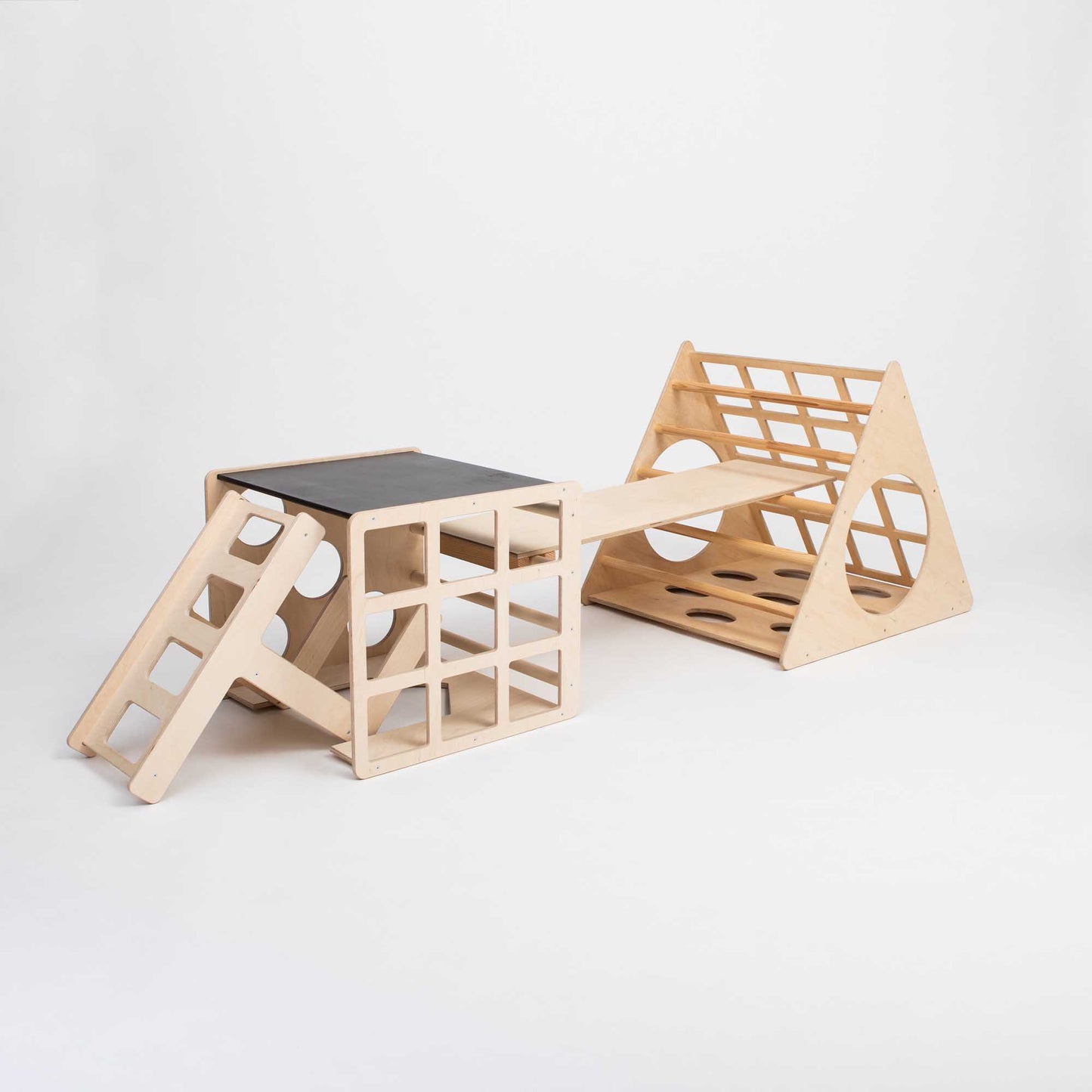 An indoor play gym featuring a Climbing triangle + 2-in-1 climbing cube / table and chair + a ramp with a ladder and a slide.