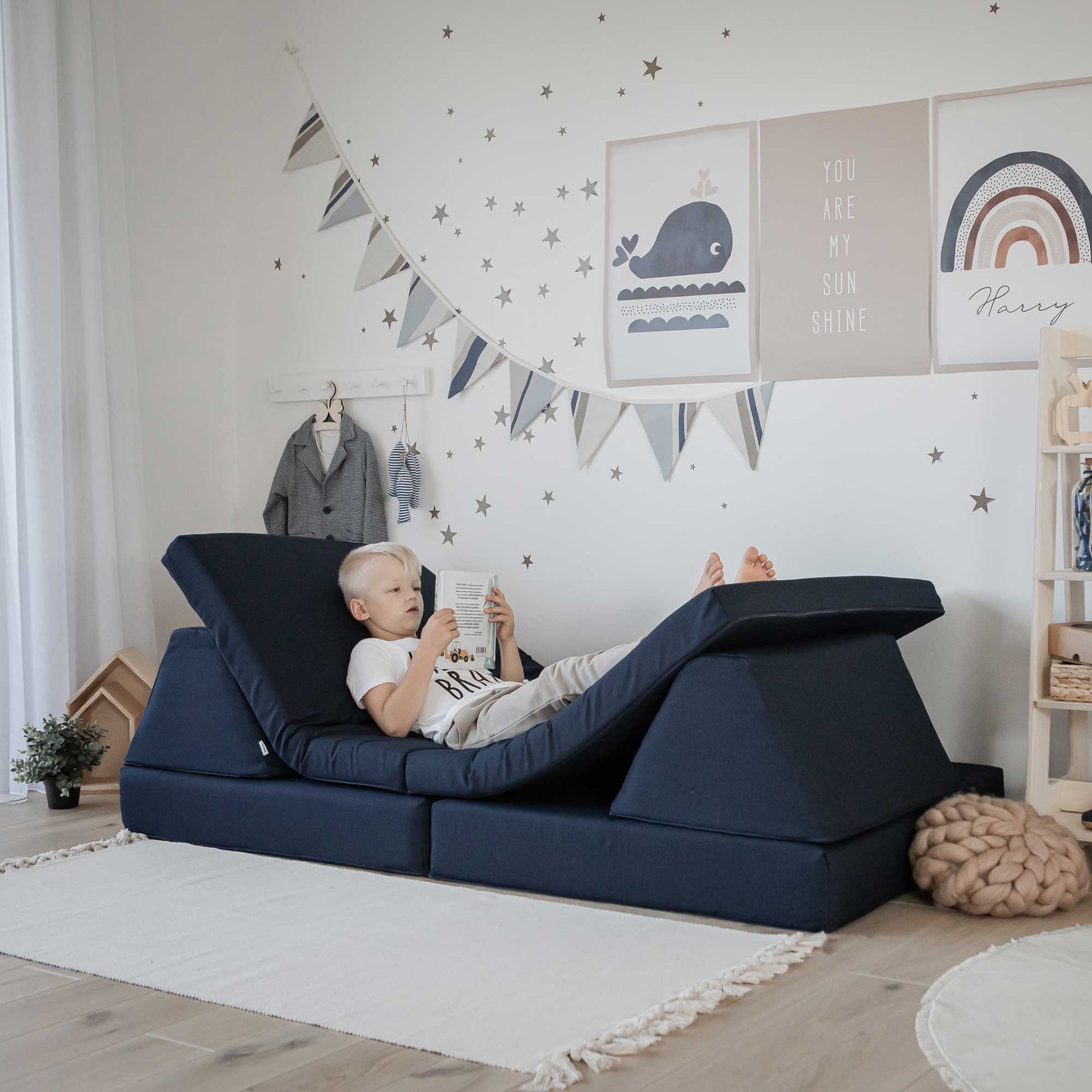 A child is laying on a blue activity play couch set in a Montessori-inspired child's room from Sweet HOME from wood.