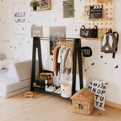 A children's room is adorned with a minimalist **Kids' clothing rack** showcasing an assortment of clothes and shoes. A woven storage basket sits nearby, while a backpack hangs on the wall along with other decorative items. To the left, a cozy couch invites relaxation, all contributing to ample dress-up storage in the space.