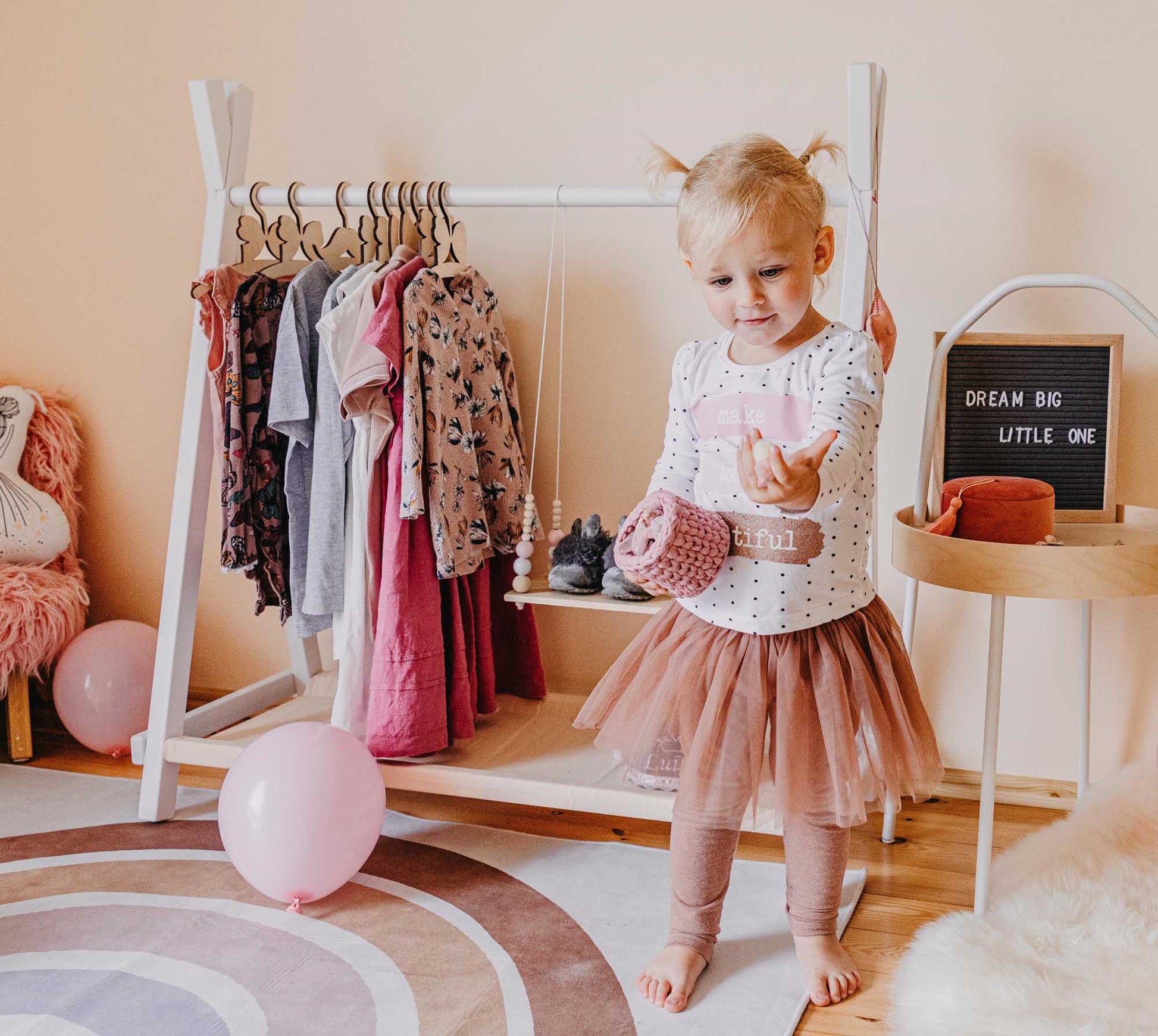 A little girl in a pink tutu standing in front of a Sweet Home From Wood Kids' clothing rack with storage.