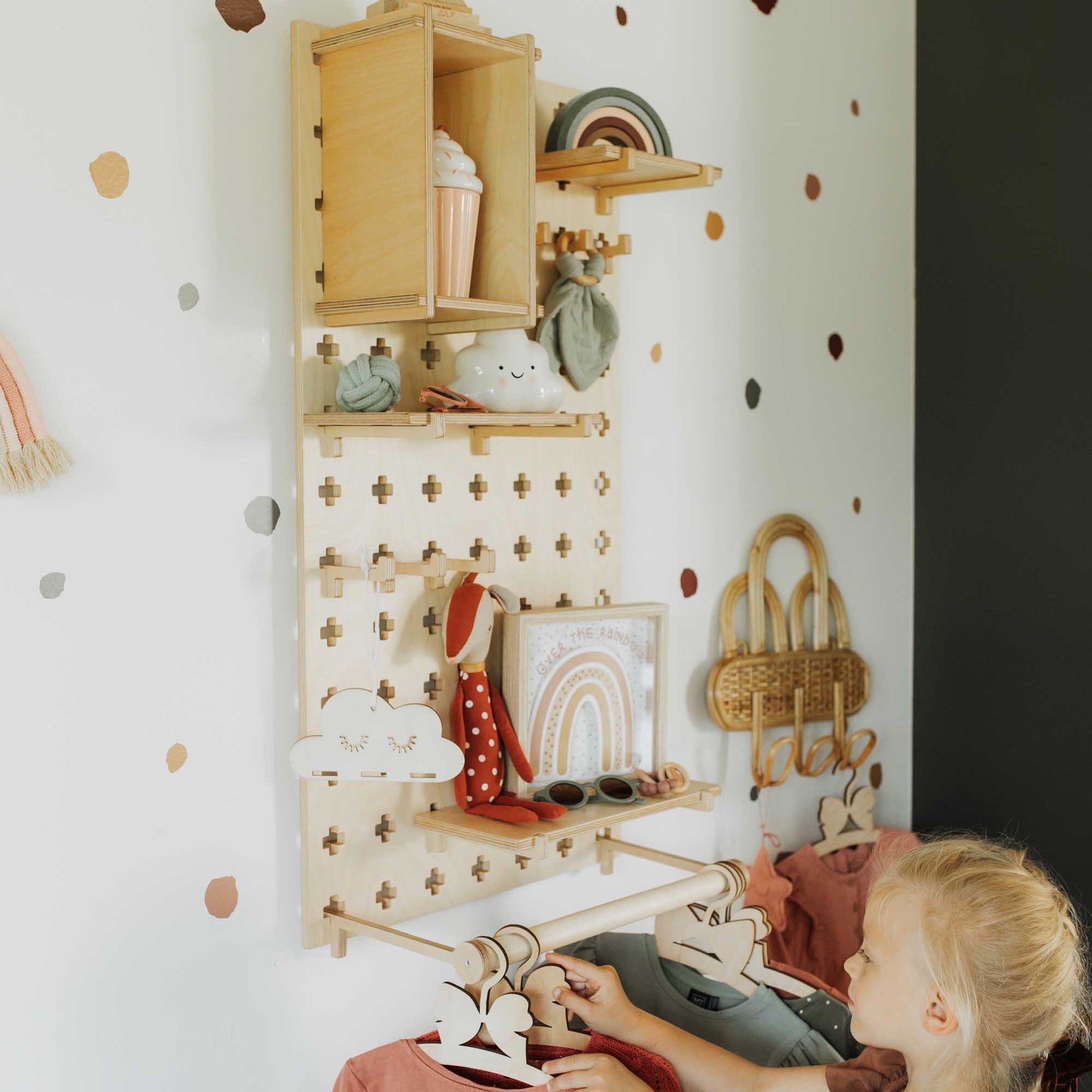 A little girl is sitting on a bed in a room with polka dot walls, surrounded by floating shelves made from Sweet HOME from wood Pegboard with Clothes Hanger.