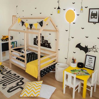 A boy's bedroom featuring a wooden house bed on legs with a fence and a batman theme.