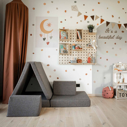 A child's room with polka dot walls, a teepee, a shelf with books and toys, and a sign saying "It's a beautiful day." The floor has a gray play couch and various toys, complemented by a Large Pegboard Floating Display Shelf for an organized storage solution.