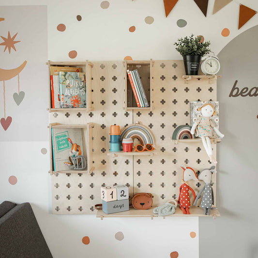 Wall-mounted wooden shelves decorated with books, toys, a clock, and a plant serve as an excellent home or office organizer. A "312 days" block calendar is displayed amidst other colorful children's items. The background wall features playful decals and an efficient Large Pegboard Floating Display Shelf set for additional storage solutions.