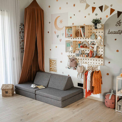 A cozy children's room with a gray sofa, a Large Pegboard Shelf with Clothing Rack for hanging clothes, floating shelves, and a small play tent in the corner. The wall is decorated with polka dots and various colorful items, making for customizable layouts perfect for your little one's imagination.