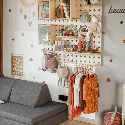 A children's room with a gray sofa, a beige canopy, floating shelves holding toys and books, a Large Pegboard Shelf with Clothing Rack displaying children's clothes, and decorative wall decals offers customizable layouts to suit any child's needs.