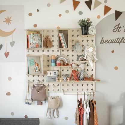 Children's room with a Large Pegboard Shelf with Clothing Rack holding toys, books, and decor, including a moon mobile, a clock, a rainbow ornament, and clothes on hangers. Polka dot walls and a garland add a playful touch. Floating shelves offer customizable layouts to keep the area neatly organized.