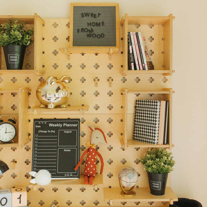 A Large Pegboard Shelf with Floating Shelves displaying a weekly planner, potted plants, books, a golden piggy bank, a clock, a globe, a toy, and a letter board reading "SWEET HOME FROM WOOD." This stylish wooden shelf provides premium storage solutions for customizable layouts.