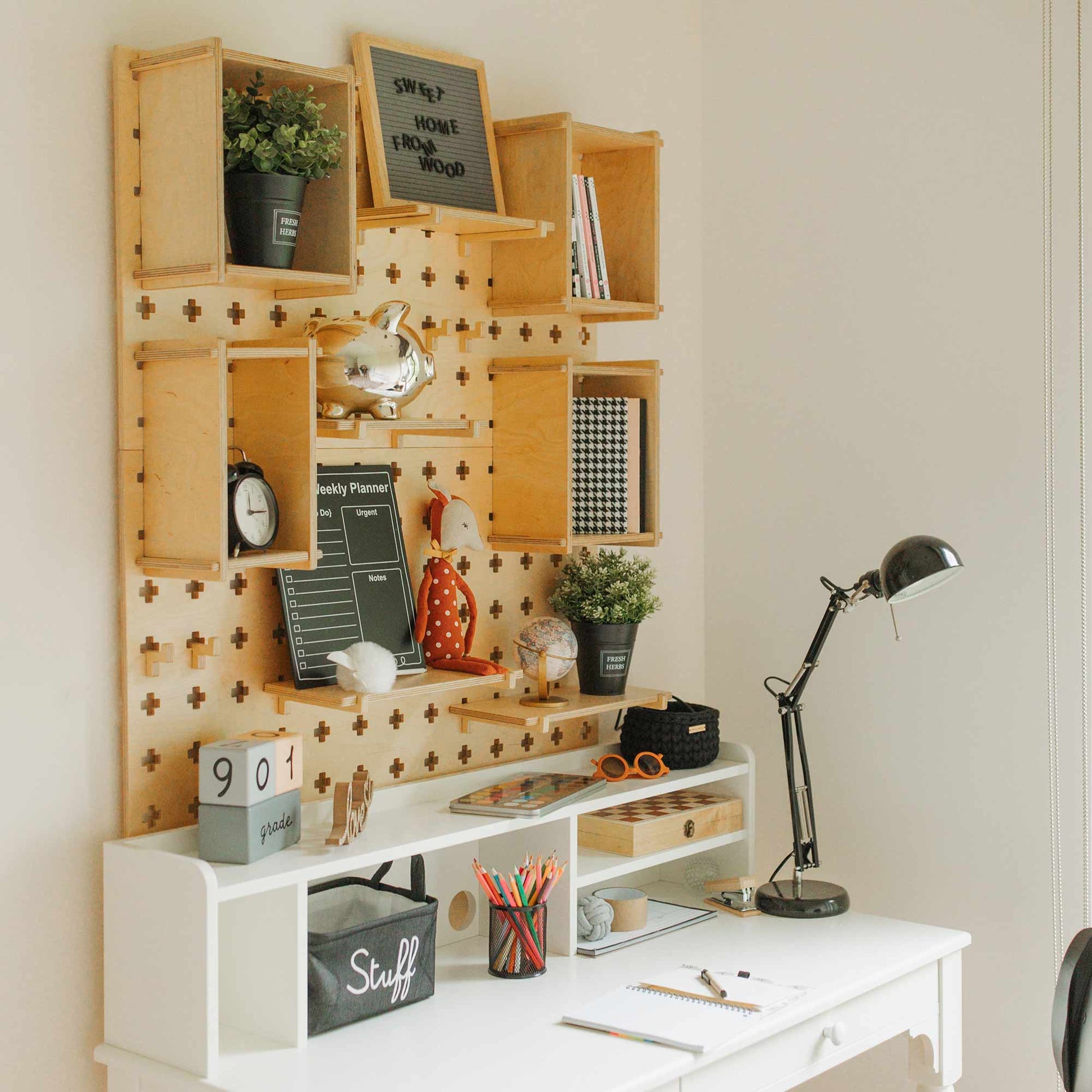 A neatly organized workspace with a white desk, a Large Pegboard Shelf with Floating Shelves mounted on the wall holding various items, potted plants, a lamp, books, and office supplies.