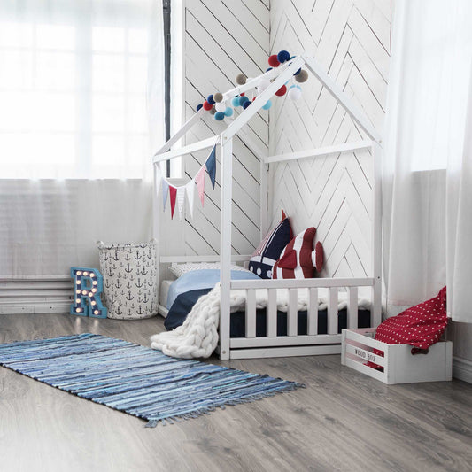 A Montessori-inspired sleep haven, featuring a wooden floor and a cozy Sweet Home From Wood toddler house bed with a headboard and footboard.