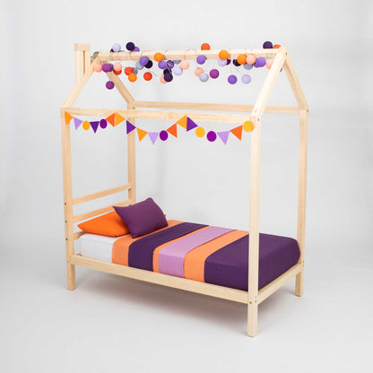 Kids' raised house bed with purple and orange pom poms.