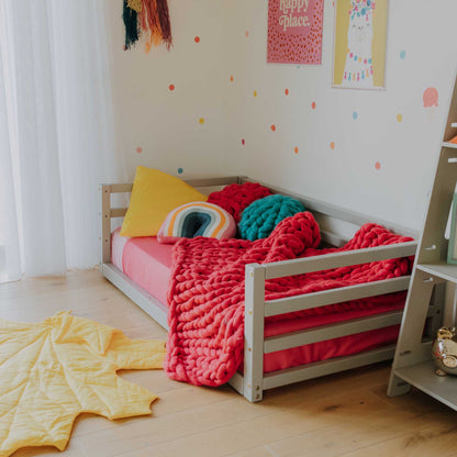 A child's room with a Sweet Home From Wood children's floor level bed with 3-sided safety rail and a shelf.