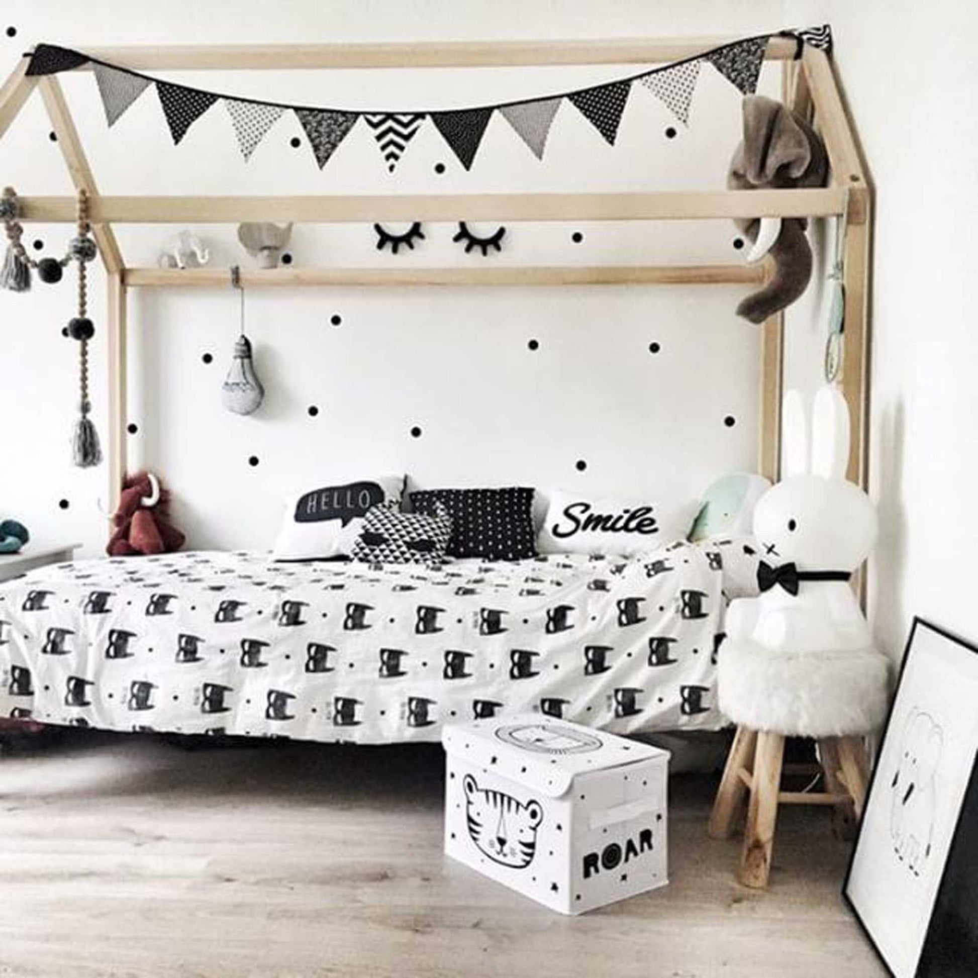 A black and white children's room with polka dots and a Wooden house bed on legs, featuring a raised house bed on legs.