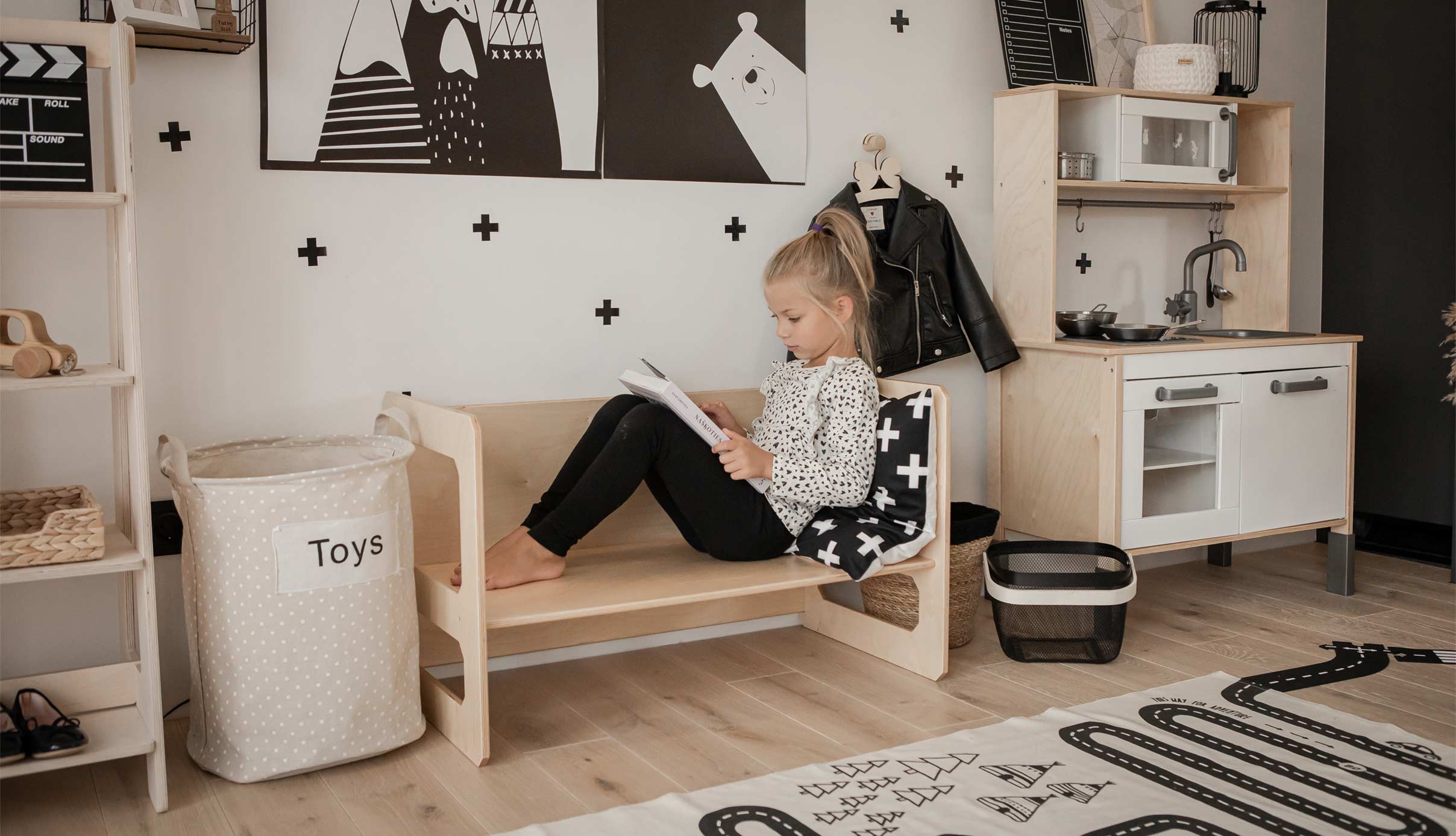 A black and white playroom with a little girl reading on a bench.