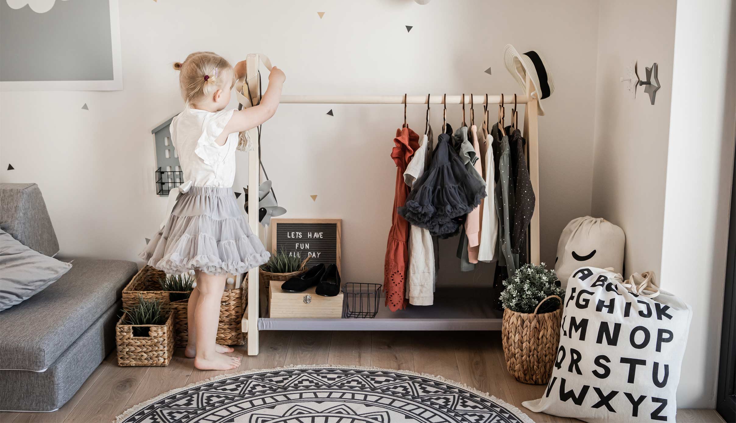 A little girl standing in front of a clothes rack in her room.