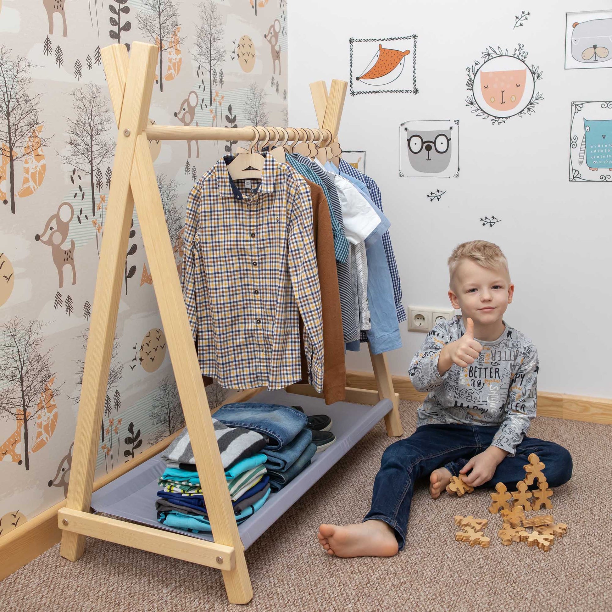 A young boy sitting in front of a "Kids' clothing rack with storage" from Sweet Home From Wood.