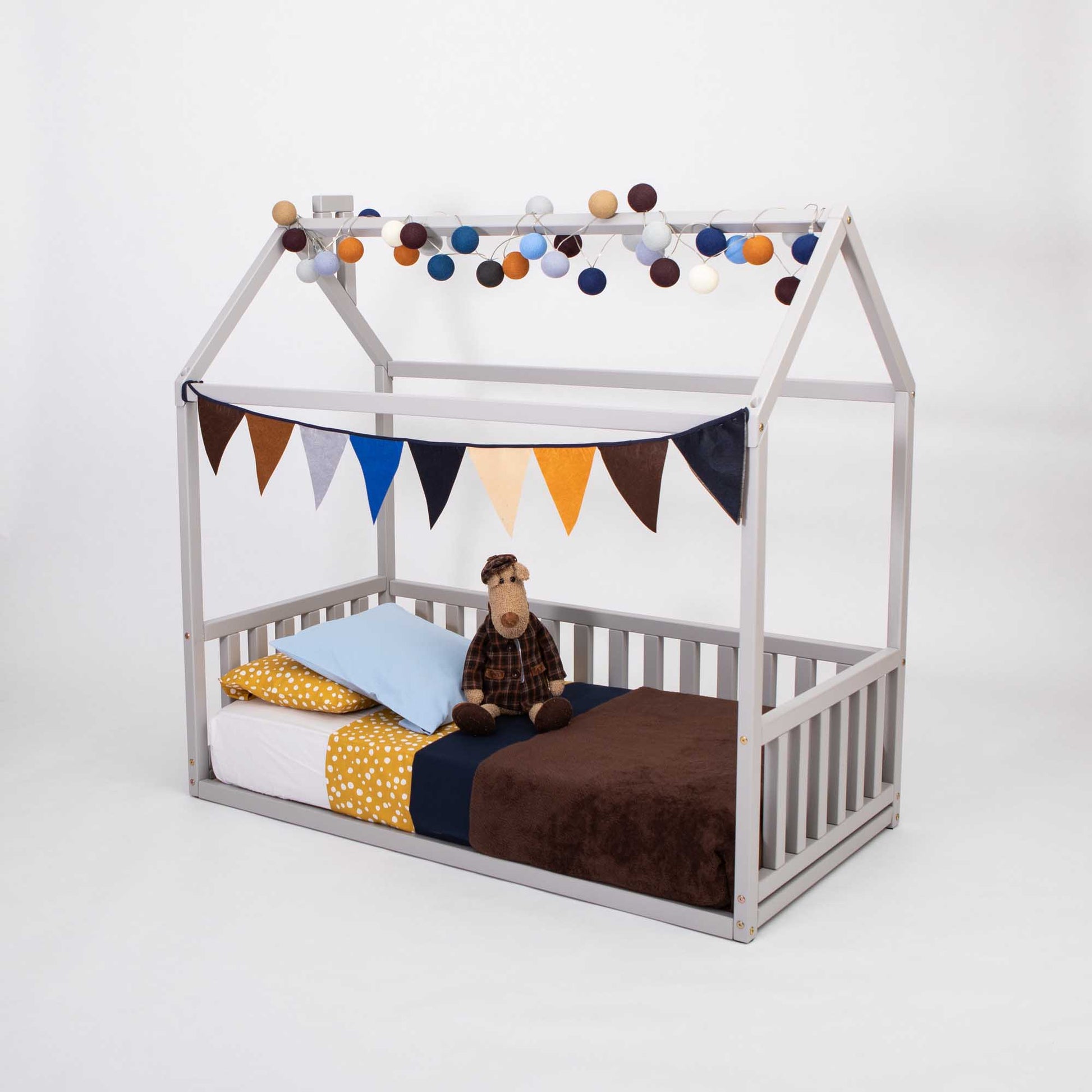 A preschool bed adorned with bunting and cuddly stuffed animals, creating a cozy sleep haven in the Sweet Home From Wood Kids' house-frame bed with 3-sided rails.