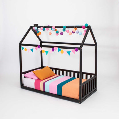 A Sweet Home From Wood Kids' house-frame bed with 3-sided rails with colorful pom poms hanging from it.