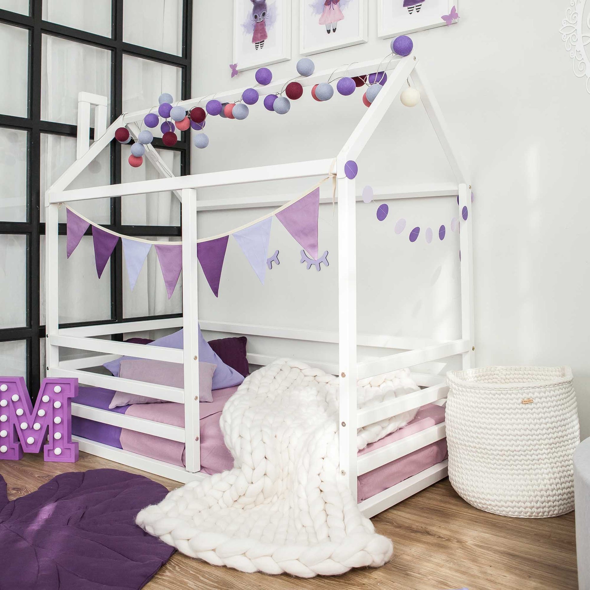 A child's bedroom with a floor level house bed with a horizontal fence for kids, adorned with purple and white decorations.