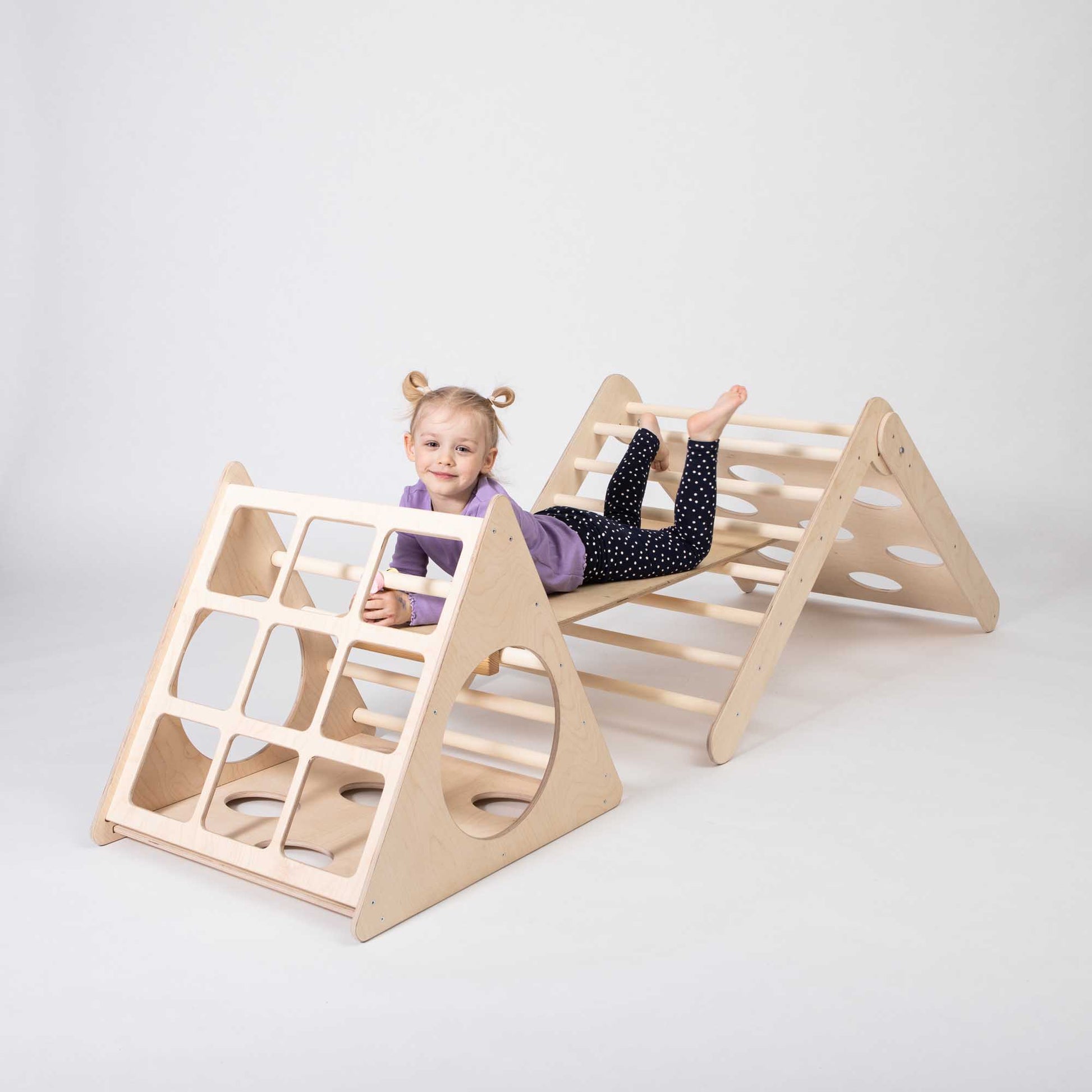 A girl joyfully playing on a Montessori climber set, featuring two distinct triangle climbers and an accompanying ramp, providing a diverse and engaging play environment for children.