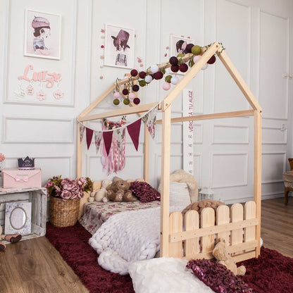 A girl's room with a Montessori house-frame bed with a picket fence headboard and footboard, teddy bears, and a low platform bed.