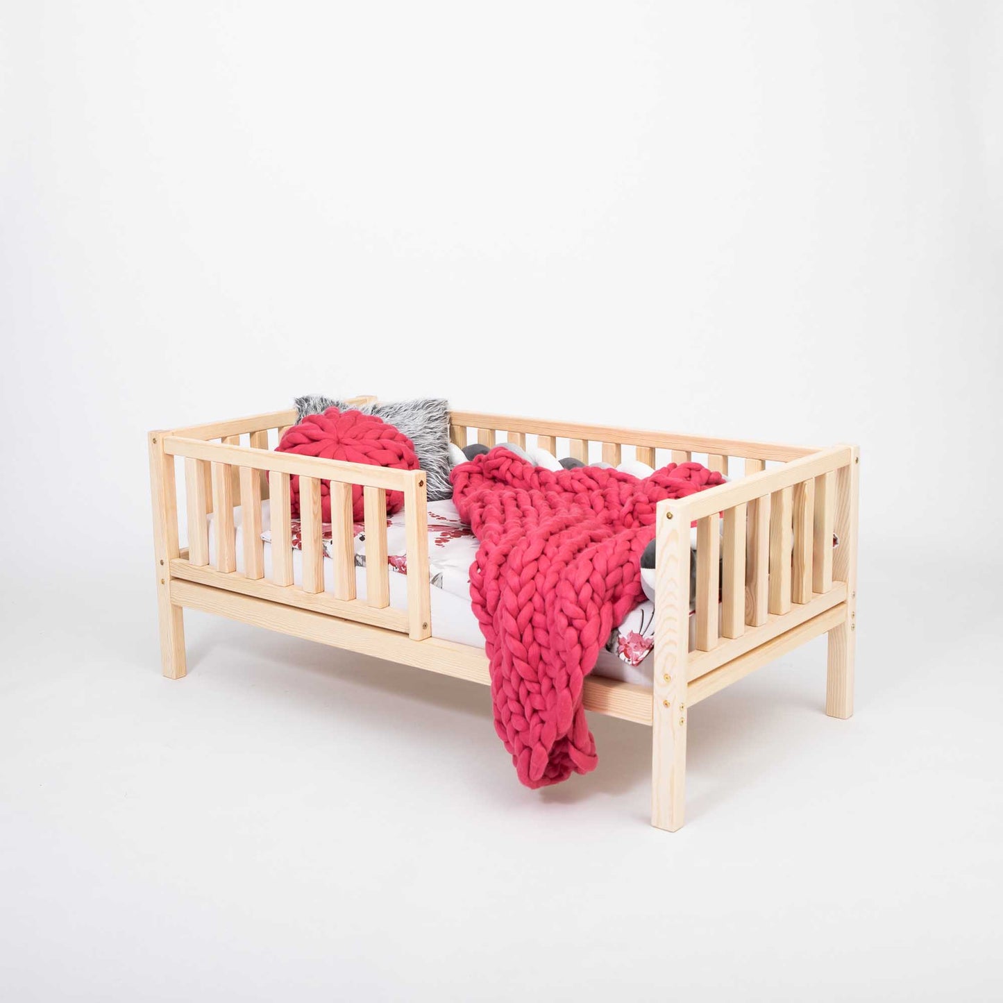 A long-lasting Sweet Home From Wood 2-in-1 toddler bed on legs with a vertical rail fence, adorned with a pink blanket.
