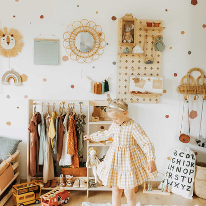 A girl in a yellow dress standing next to Sweet HOME from wood Floating Shelves Pegboard, with polka dots decorating the room.