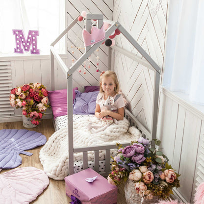 A preschool girl is sitting in a cozy Sweet Home From Wood Kids' house-frame bed with 3-sided rails adorned with flowers.