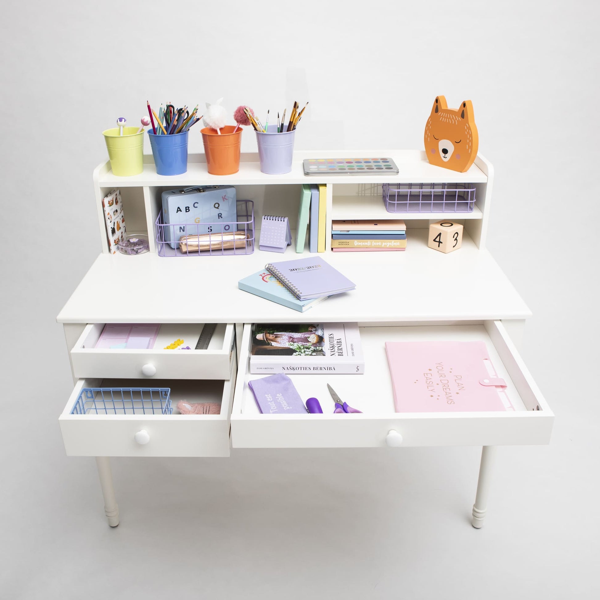 A neat, versatile children's Pedestal desk with open drawers displaying school supplies, books, and colorful stationery against a white background.