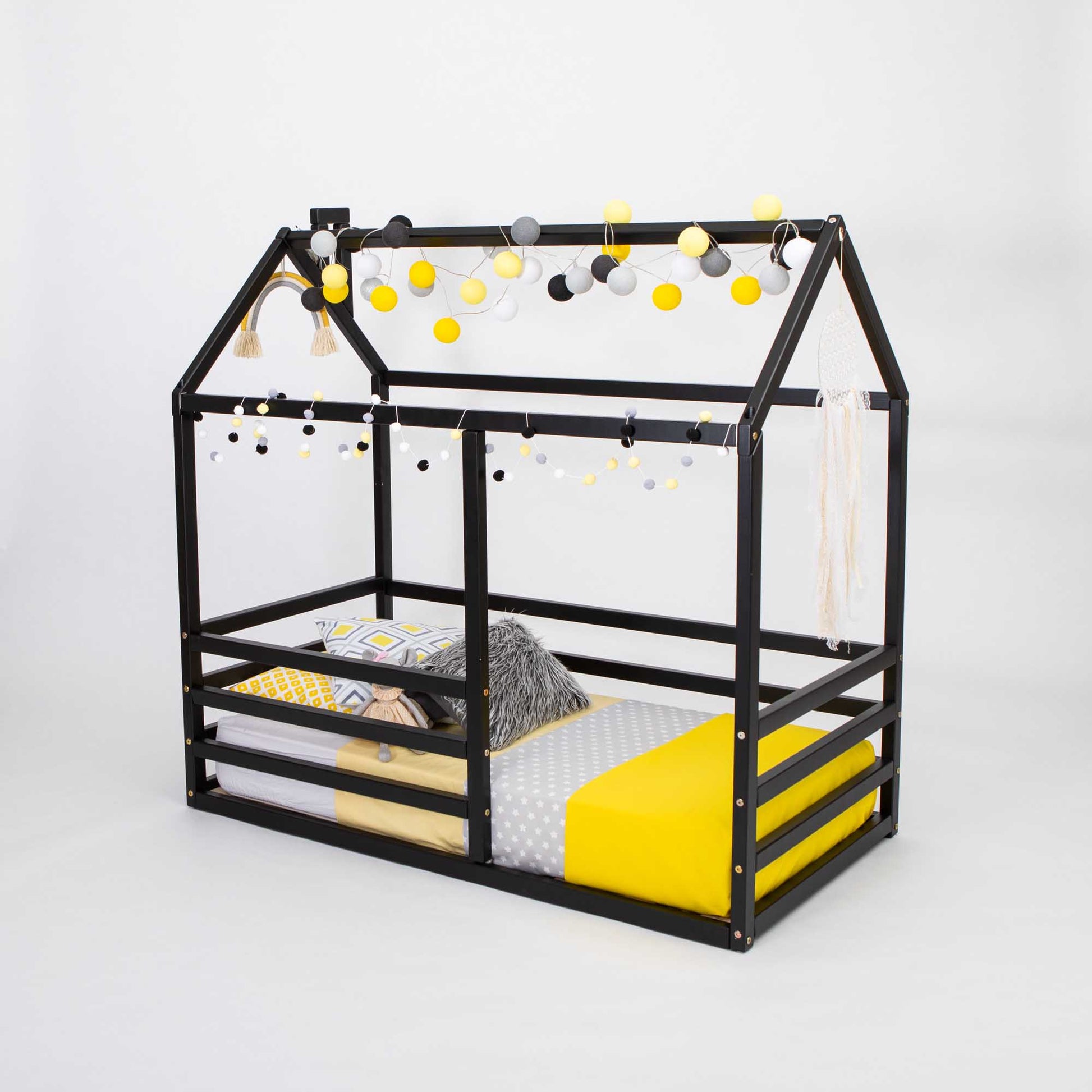 A black floor level house bed with a horizontal fence with yellow decorations.