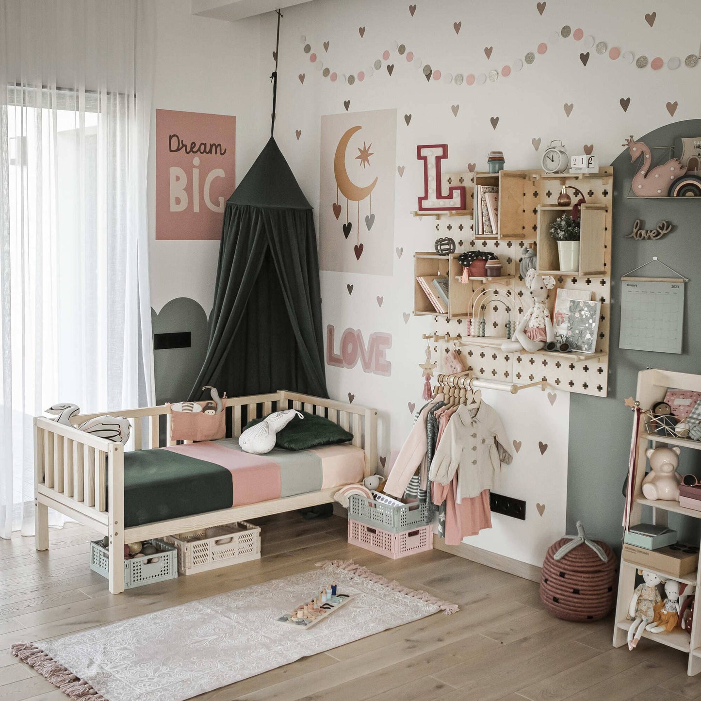 A well-decorated children's bedroom with a solid wood Kids' platform bed on legs featuring 3-sided rails, toys, shelves, books, and wall decor including a canopy adorned with moon and heart patterns, as well as the words "DREAM BIG" and "LOVE," offering both independence and security.