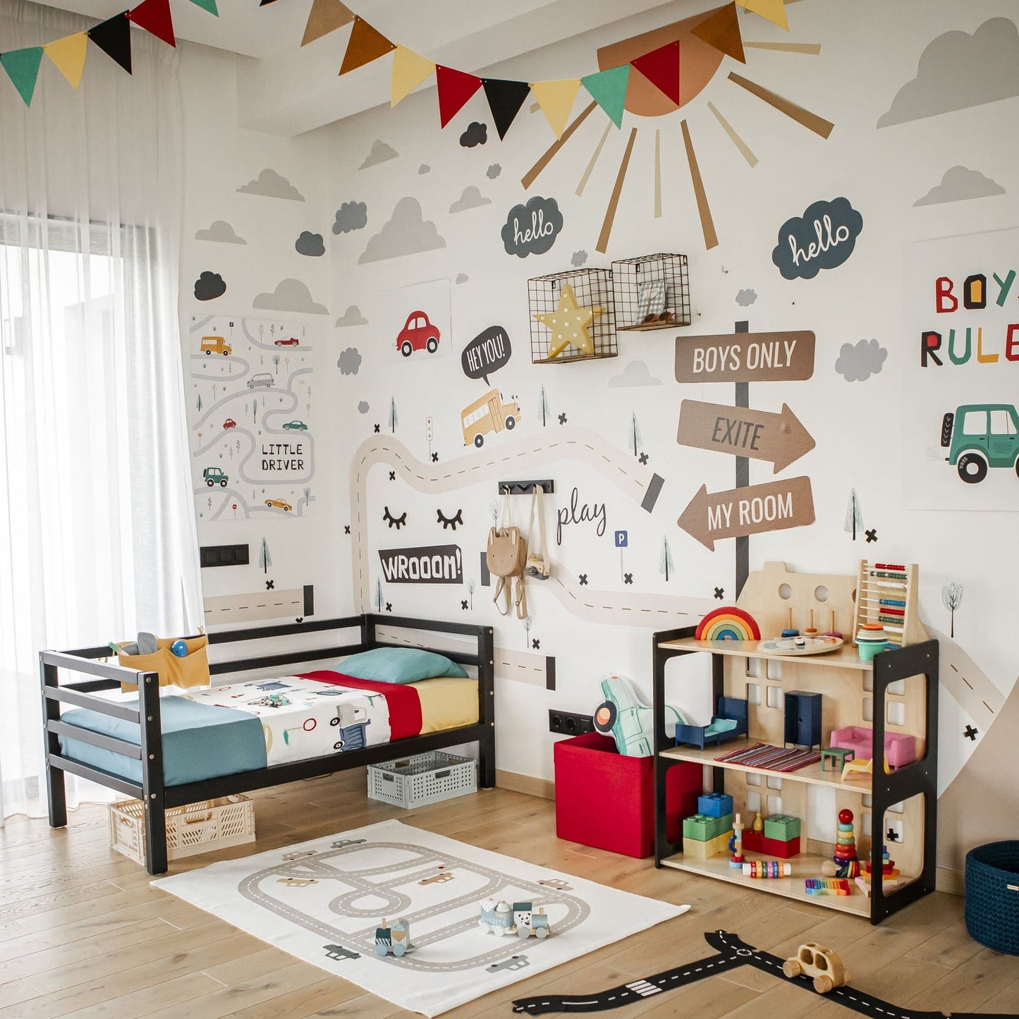 A children's bedroom featuring transportation-themed wall stickers, a loft bed, a practical 2-in-1 doll house and Montessori shelf filled with toys, colorful bunting hanging from the ceiling, and a play mat with a road design on the floor.