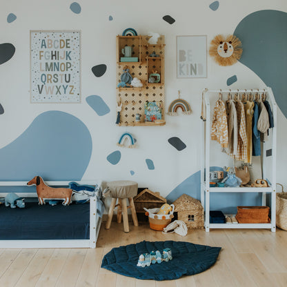 Children's room with blue-themed decor, including a small bed, a wooden shelf with toys, a clothing rack, and wall art featuring an alphabet print and "Be Kind" message. A Pegboard Wall Shelf adds versatile organization options for all their little treasures.