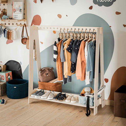 An A-frame kids' clothing rack in a playroom, featuring various clothes on hangers, shelves with bins of toys and accessories, and a mural on the wall, offers excellent closet organization.